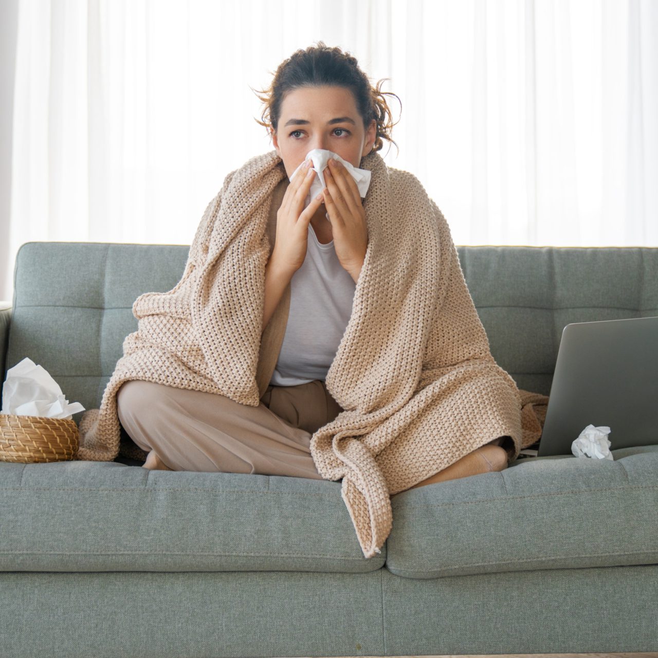 Woman sitting on lounge with tissue and blanket